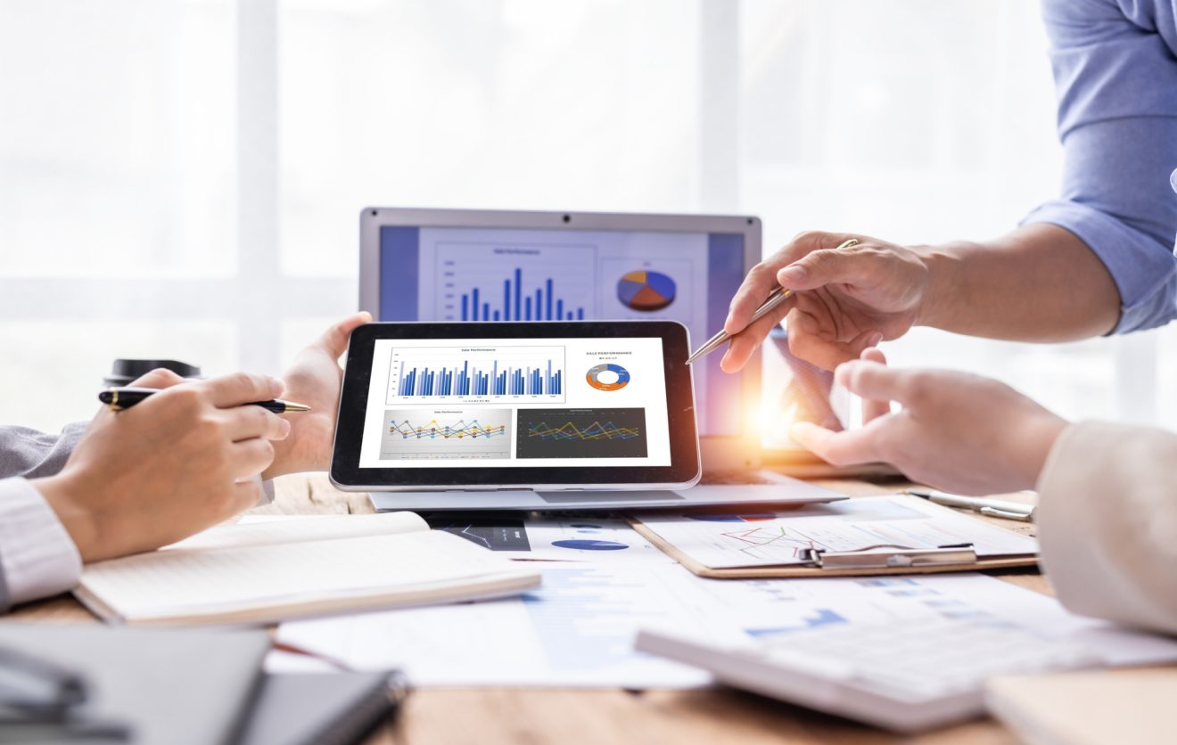 People at a desk reviewing graphs and charts on a tablet and laptop screen