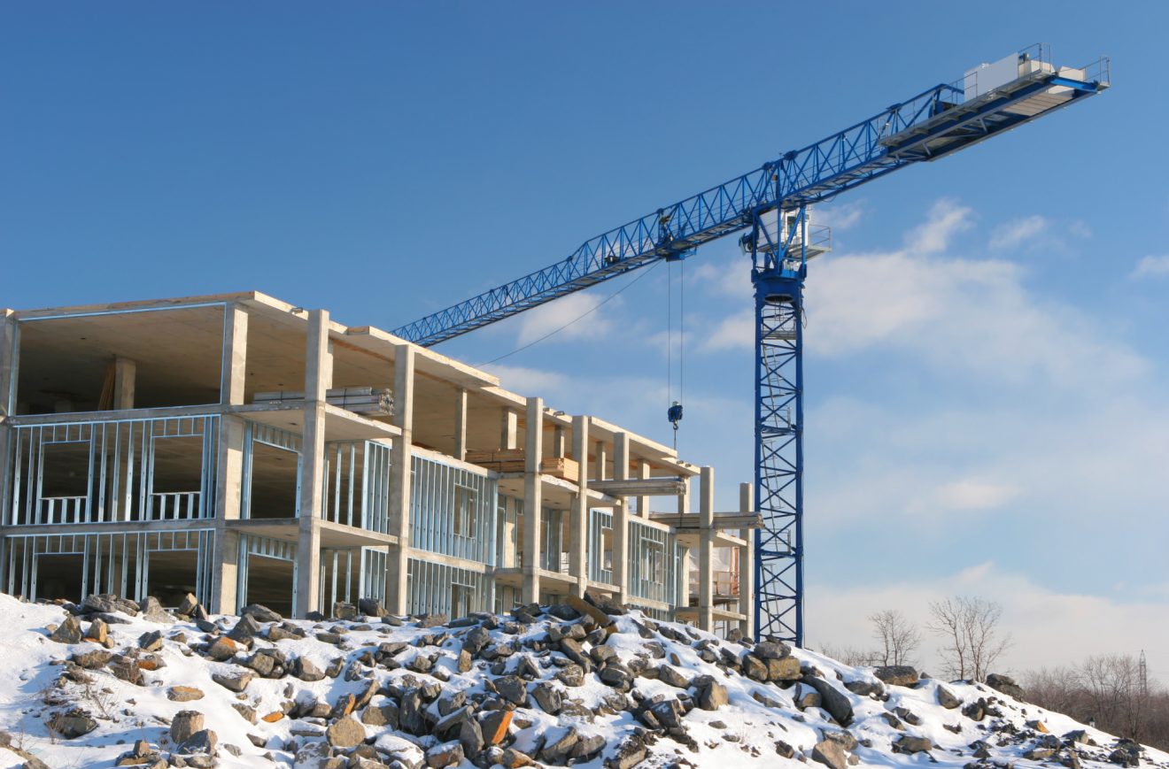 A building in progress, with a crane and a snowy foreground
