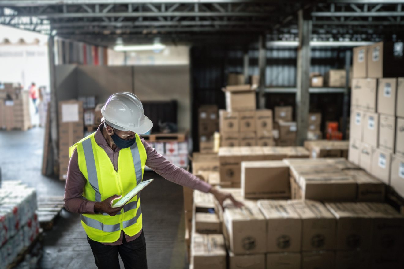 Person in a hardhat and yellow safety vest reviewing products to be shipped