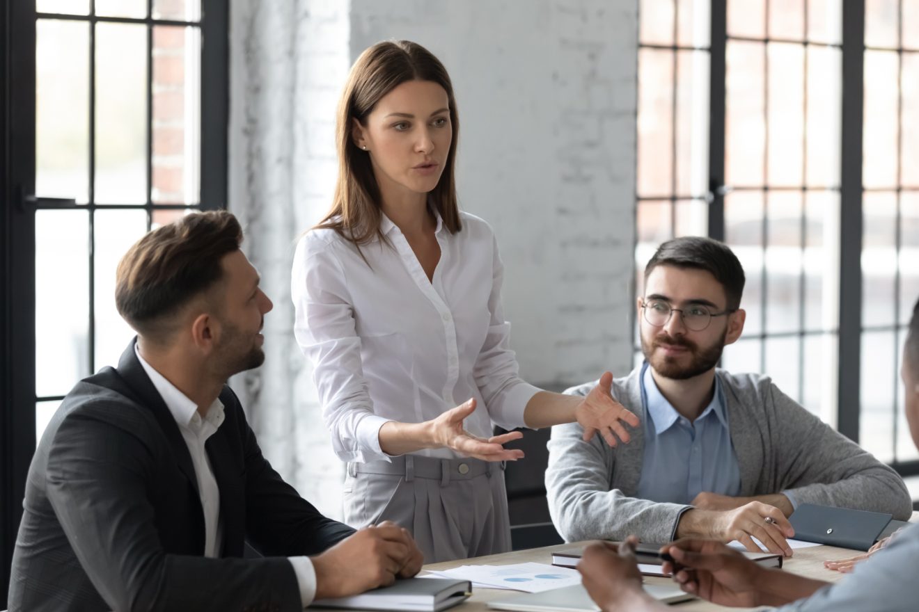 Woman standing at desk talking while two men listen