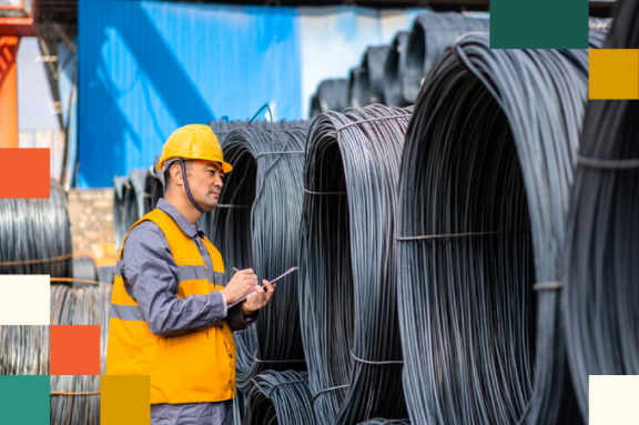 man is reflective vest and hard hat examines large rolls of wire on construction site